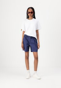 White cotton t-shirt with crew neckline, paired with navy blue cargo shorts featuring an elastic waistband and side pockets. White sneakers.