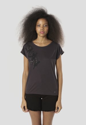 Camiseta de manga corta de color gris oscuro con un diseño floral en negro, que presenta bordados texturizados y un escote redondeado. Combinada con pantalones cortos negros.