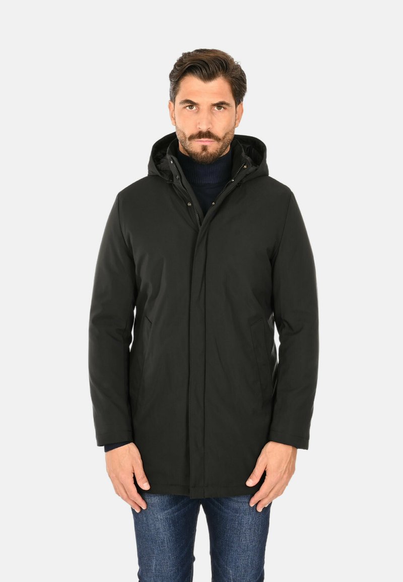 Giacca con cappuccio nera, dotata di chiusura con zip, tessuto morbido, due tasche laterali e un taglio leggermente più lungo, abbinata a jeans blu.