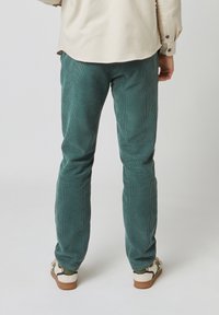 Groene corduroy broek met een ribbelstructuur, slim fit, en een achteraanzicht. In combinatie met beige en groene sneakers.