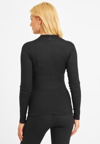 Woman with blonde hair wearing a fitted black ribbed long-sleeve top and matching black pants, shown from the back on a white background.