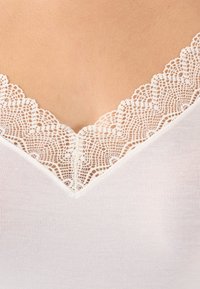 Top bianco con scollatura a V profonda, decorato con una elegante rifinitura in pizzo che mette in risalto la texture a costine del corpo del capo.