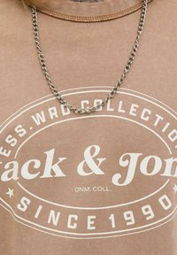 Braunes Baumwoll-T-Shirt mit weißen Textgrafiken, Rundhalsausschnitt und einer silbernen Kettenhalskette obendrauf, mit einer glatten Textur.