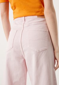 Pantalon en denim rose à coupe décontractée, avec deux poches arrière et un design de couture subtil. La ceinture est ornée d'une touche de cuir marron.