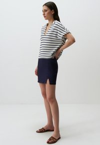 Top a righe a V in bianco e blu navy, abbinato a una mini gonna blu navy con uno spacco frontale. Sandali marroni con cinturino completano il look.