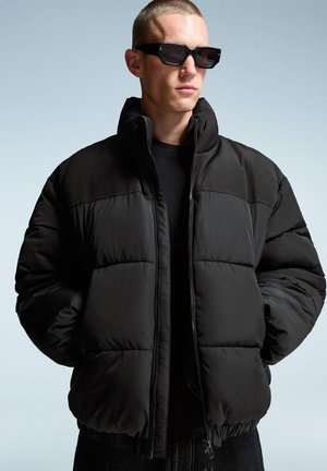 Schwarze Daunenjacke mit hohem Kragen, gestepptem Design und elastischen Bündchen, ausgestattet mit einem Reißverschluss und einer glatten, matten Oberfläche.