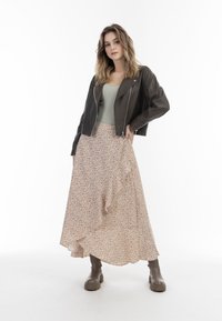 Brun läderkort jacka, ljusgrön figurnära topp, flödande beige kjol med röd blommönster, och bruna ankelstövlar.