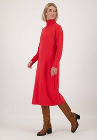 Rode coltrui jurk van zachte stof met lange mouwen, een losse pasvorm en een knielange uitvoering, gecombineerd met bruine haklaarzen.