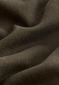 Gros plan sur un tissu brun froissé avec une fine texture côtelée diagonale créant des ombres et plis doux.