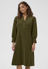 Green corduroy dress with a V-neck, button closure, and three-quarter sleeves. Features a relaxed fit and knee-length hemline.