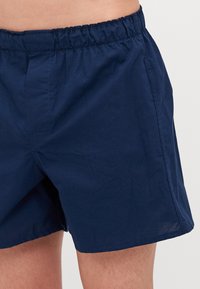 Mørkeblå shorts laget av lett materiale, med elastisk liv, sidelommer og en avslappet passform med minimale tekstur detaljer.