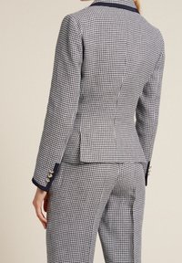 Chaqueta de traje a medida en patrón de cuadros vichy azul marino y blanco, con diseño ajustado, cuello con muesca y puños abotonados. Tejido texturizado.