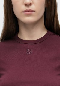 Bordoopunane liibuv T-särk ümarate kaelusega, mille rinnal on sama värvi tikitud "HUGO" logo, sile tekstuur.