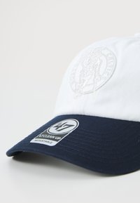 Adjustable cap featuring a white front and navy blue brim. Embroidered logo on the front and a stitched label on the side. Textured fabric.