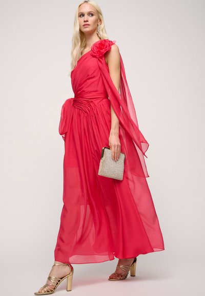 Long, flowing dress in sheer, bright pink fabric with a one-shoulder design, floral accent, gathered waist, and a matching clutch. Gold heels.