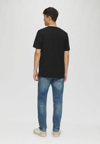 Black cotton t-shirt with short sleeves, crew neck, and a relaxed fit, paired with blue denim jeans and beige sneakers.