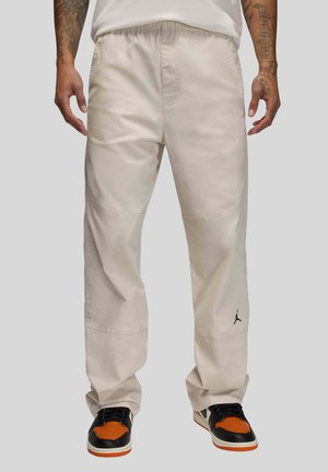 Beige pants with an elastic waistband, wide legs, subtle stitching details, and a small black Jordan logo on the lower left leg.