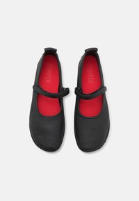 Mustat nahkaiset Mary Jane -kengät, joissa on pyöristetty kärki, punainen sisäpohja ja säädettävä hihna. Liukas pinta, jossa on minimaalista muotoilua.
