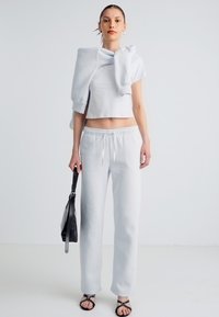 Helehall hall spordiriiete komplekt, mis sisaldab lühendatud ülaosa ja lahtiseid pükse. Materjal on pehme ja kergelt tekstureeritud. Must käekott ja sandaalid.