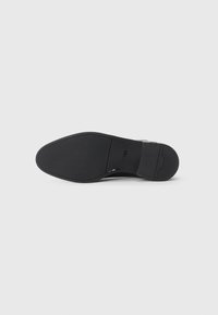 Semelle de chaussure formelle noire élégante avec un devant texturé et le mot "BOSS" embossé près du talon sur un fond clair.