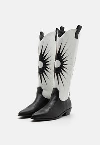 White cowboy boots with black starburst patterns and accents, featuring a pointed toe and a low heel, made from smooth leather.