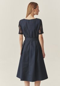 Meresinine kleit lühikeste pitsvarrukatega, istuva ülakehaosaga ja lehviva seelikuga, millel on vöökoht ja seljal tõmblukk.