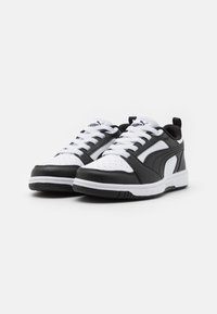 Scarpe sportive in bianco e nero con una tomaia in pelle liscia, punta perforata, suola in gomma e logo prominente sulla linguetta e sul lato.