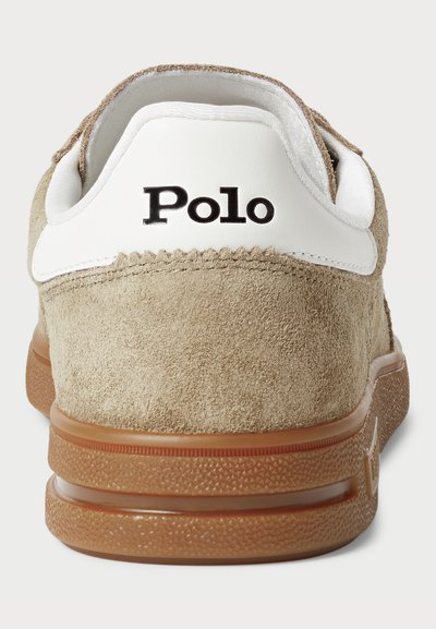 Zapatillas de ante color marrón con un talón de cuero blanco que presenta la palabra "Polo" en negro. La suela de goma es marrón con patrones texturizados.