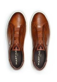 Zapatos marrones de cuero sin cordones con paneles elásticos en los laterales, suela de goma blanca y un logo negro en la lengüeta. Textura suave con un diseño minimalista.
