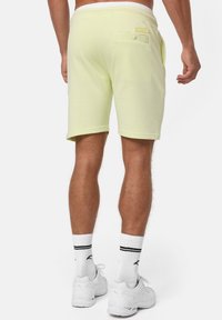 Lys gule bomuldsshorts med en baglomme og subtil branding. Har en strækbar talje og opsmøgte kanter. Bæres med hvide sokker og sko.