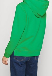 Sudadera con capucha en verde brillante, con un ajuste relajado, puños y dobladillo acanalados. Textura suave con detalles de costura visibles.