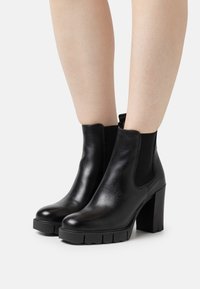 Botas de cuero negro hasta el tobillo con paneles laterales elásticos, suela texturizada gruesa y un alto tacón en bloque. Acabado suave con un ligero brillo.