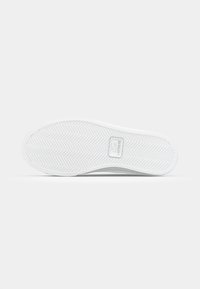 White rubber shoe sole with a herringbone tread pattern and a prominent logo detail. Smooth texture and curved edges.