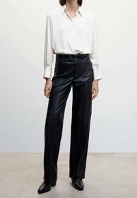 Chemise blanche à manches longues avec patte de boutonnage, associée à un pantalon en cuir noir taille haute avec une coupe droite et une ceinture.