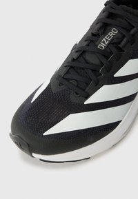 Baskets de sport noires avec une tige texturée, dotées de rayures blanches en diagonale, de lacets et d'une semelle rembourrée avec un logo discret sur le talon.