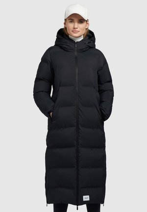 Lungo cappotto trapuntato nero con cappuccio, dotato di zip frontale, tasche laterali e una texture leggermente lucida. Etichetta bianca del marchio esposta.