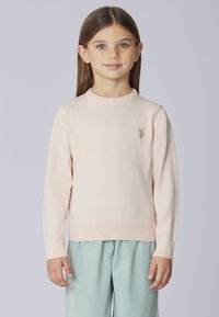 Maglione rosa chiaro lavorato a maglia con scollo rotondo e orlo a coste. Presenta un logo ricamato sul petto a sinistra. Abbinato a pantaloni azzurri.