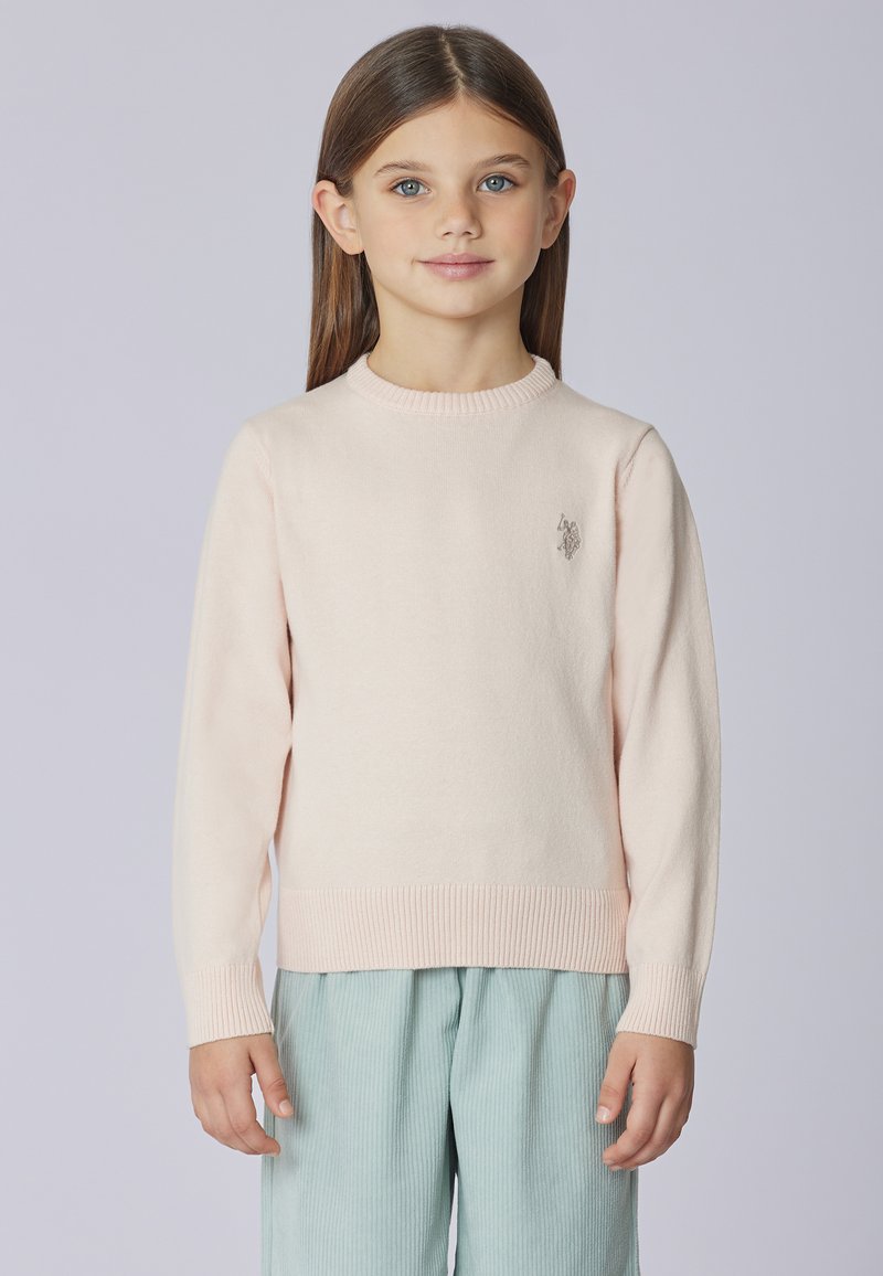 Maglione rosa chiaro lavorato a maglia con scollo rotondo e orlo a coste. Presenta un logo ricamato sul petto a sinistra. Abbinato a pantaloni azzurri.