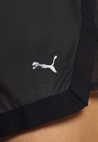 Pantalones cortos deportivos negros con un logo blanco de Puma cerca del dobladillo y un detalle de panel de malla en el costado.