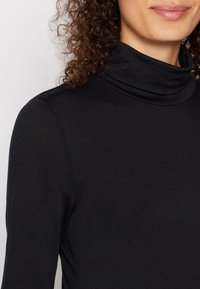 Black turtleneck top made of soft, textured fabric. Features a high collar and long sleeves, with a fitted silhouette.
