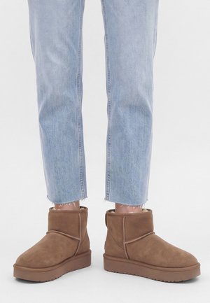 Jean bleu clair coupé au-dessus des chevilles, associé à des bottines en suède marron avec semelles plates et coutures visibles.