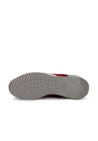 Zapatilla roja y blanca con una suela de goma gris texturizada, que presenta patrones de agarre circulares y un logo que dice "MUNCH desde 1939."
