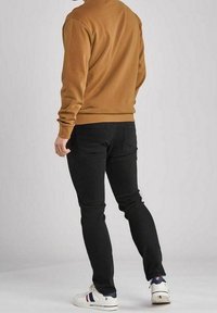 Brun sweatshirt, svarta jeans och vita sneakers. Slät tyg, passform design och enkel sömnad. Sneakers har en låg design med detaljer.