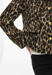 Giacca con stampa a macchie di leopardo nelle tonalità di marrone e nero, caratterizzata da bottoni dorati, due tasche frontali e un design cropped con maniche ampie.