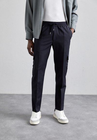 Pantaloni bleumarin cu talie elastică și șnur, având buzunare laterale și o croială slim, asortați cu adidași albi.