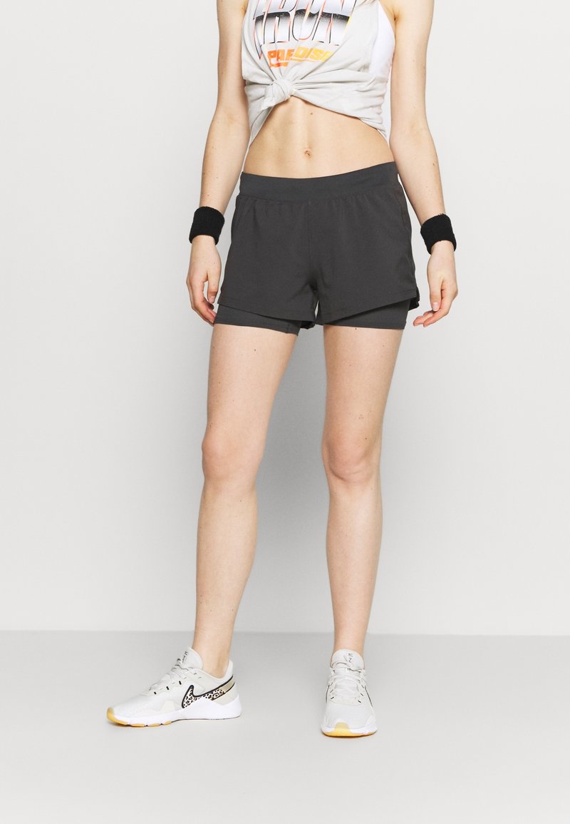 Pantalones cortos deportivos negros de corte holgado, fabricados con material ligero, con un diseño sencillo y una cintura elástica. Combinados con zapatillas blancas.