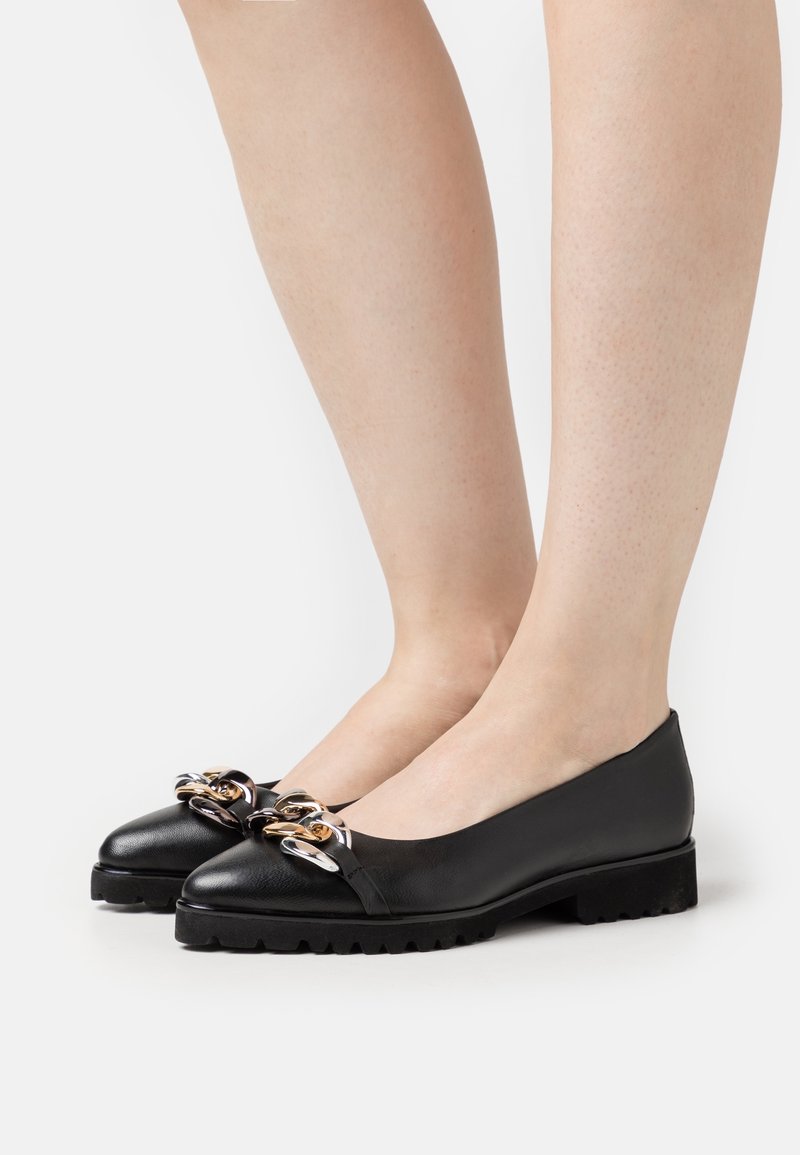 Ballerines en cuir noir avec un bout arrondi, un petit talon épais et des accents de chaîne décorative en or et en argent. Semelle texturée.