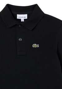 Schwarzes Poloshirt aus strukturierter Baumwolle, mit einem klassischen Kragen, drei Knöpfen und einem kleinen grünen Krokodil-Logo auf der linken Brust.