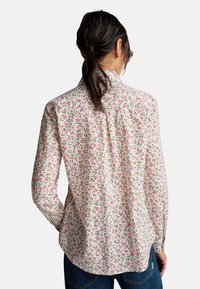 Camicia floreale, sfondo bianco con piccoli fiori rosa e foglie verdi. Maniche lunghe, colletto e orlo curvato. Design classico con bottoni.