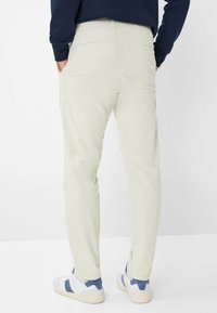 Pantaloni in velluto a coste verde chiaro con taglio dritto, dotati di tasche posteriori e abbinati a sneakers bianche e dettagli blu.